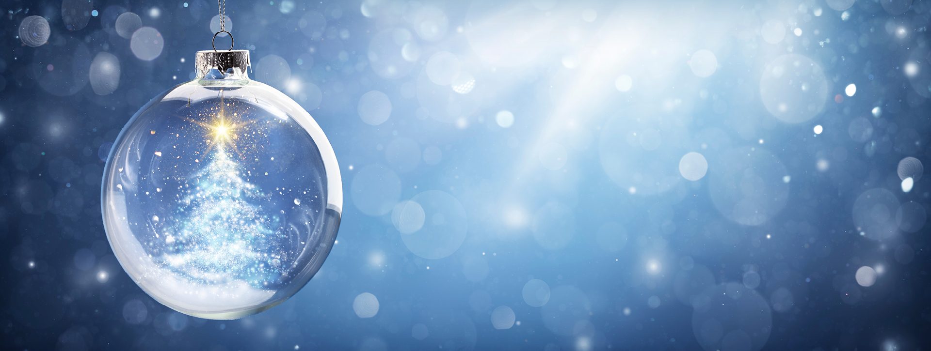 Eine transparente Weihnachtskugel schimmert im Licht und zeigt einen glitzernden, weißen Weihnachtsbaum mit einem leuchtenden Stern an der Spitze. Der Hintergrund ist sanft in Blau- und Silbertönen gehalten und ergänzt die festliche Atmosphäre.