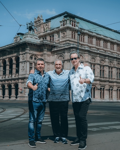 Drei Männer posieren vor dem Gebäude der Wiener Staatsoper