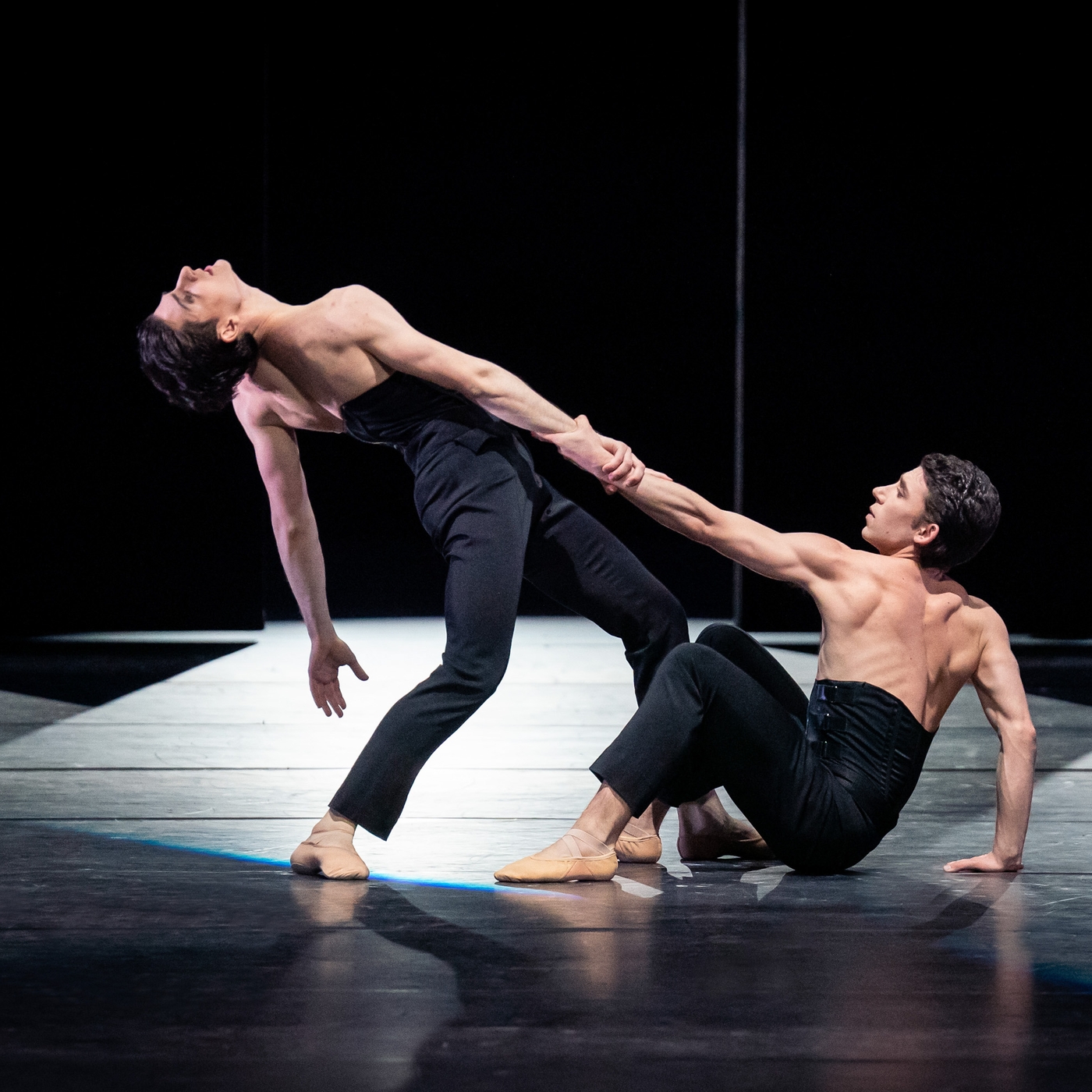 Zwei Balletttänzer tanzen auf einer dunklen Bühne.