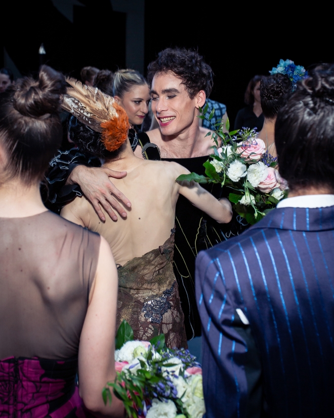 Zwei Balletttänzer*innen umarmen sich. Eine der beiden Personen hält einen Blumenstrauß.