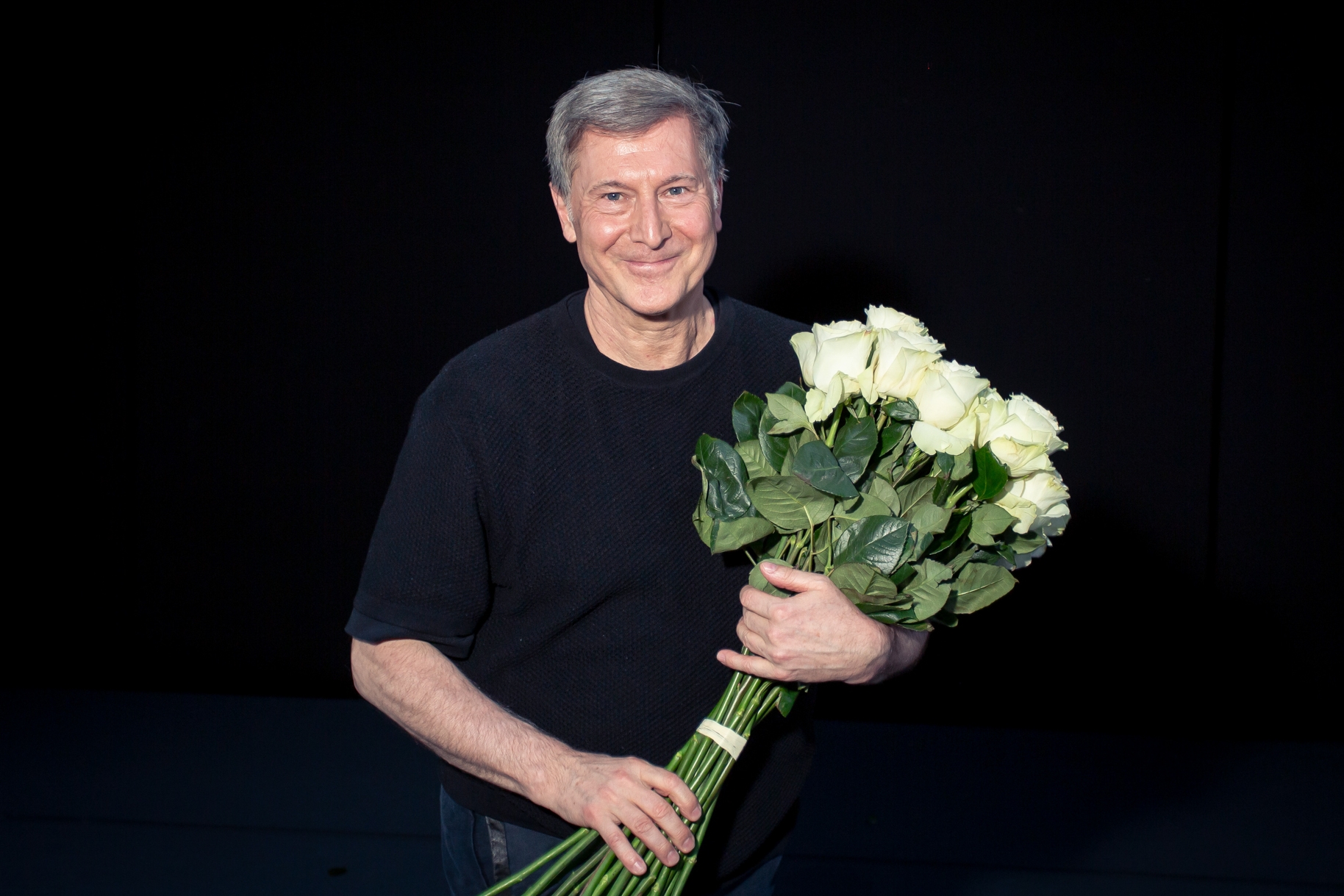 Martin Schläpfer freut sich und hält einen großen Strauß weißer Rosen.