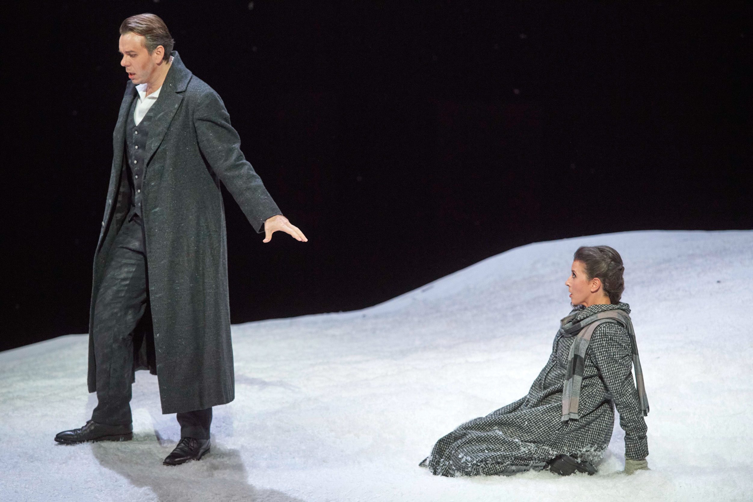 Eine Frau kniet auf dem Boden, vor ihr wendet ihr ein dunkel gekleideter Mann den Rücken zu