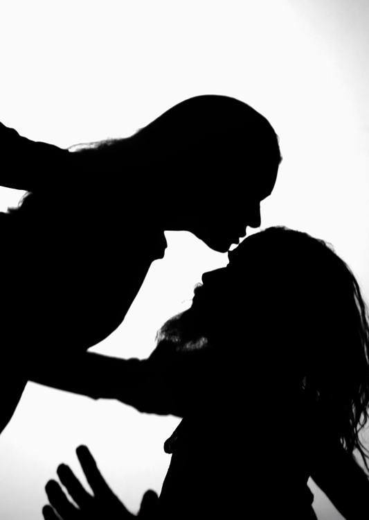 Zwei Personen sind in Silhouette dargestellt, während sie sich nahe kommen. Die dargestellte Szene vermittelt Intimität und Zuneigung durch die Annäherung der Köpfe. Der Hintergrund ist hell, was den Fokus auf die Körperhaltungen und Gesten der beiden Personen verstärkt.