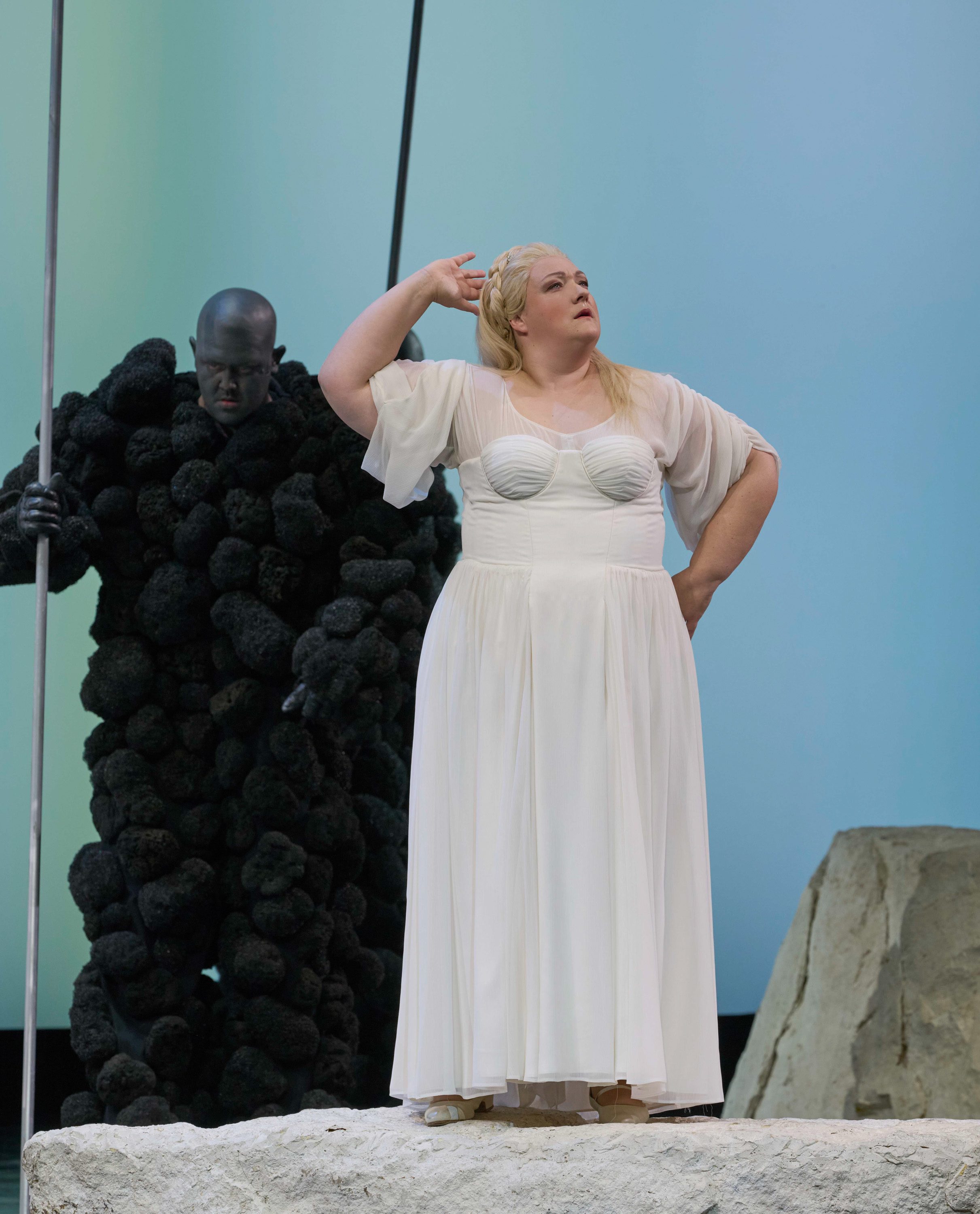 Eine Frau in einem weißen Kleid neben einer dunklen, wolkenartigen Figur.