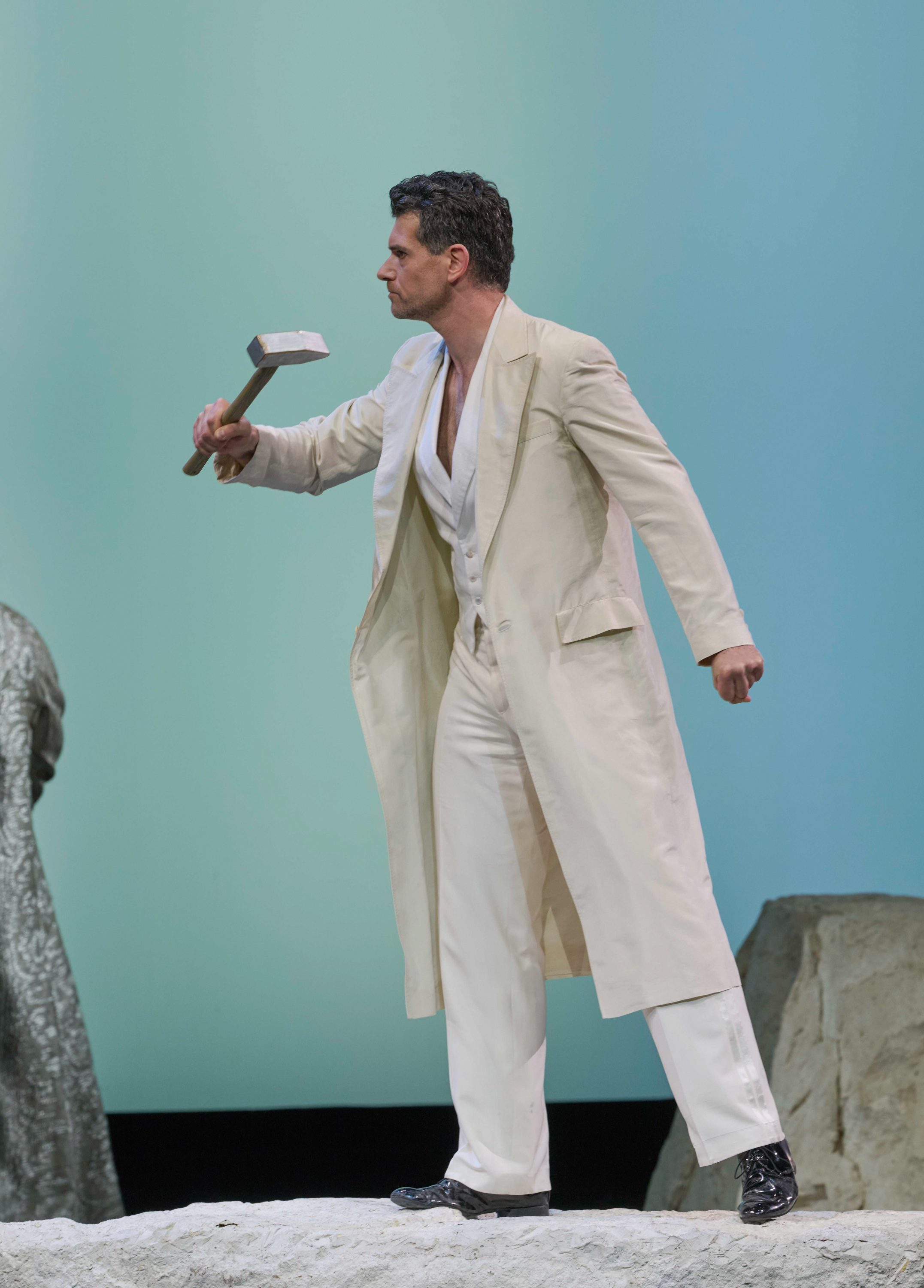 Ein Mann in einem weißen Anzug hält einen Hammer in der Hand und schaut zur Seite.