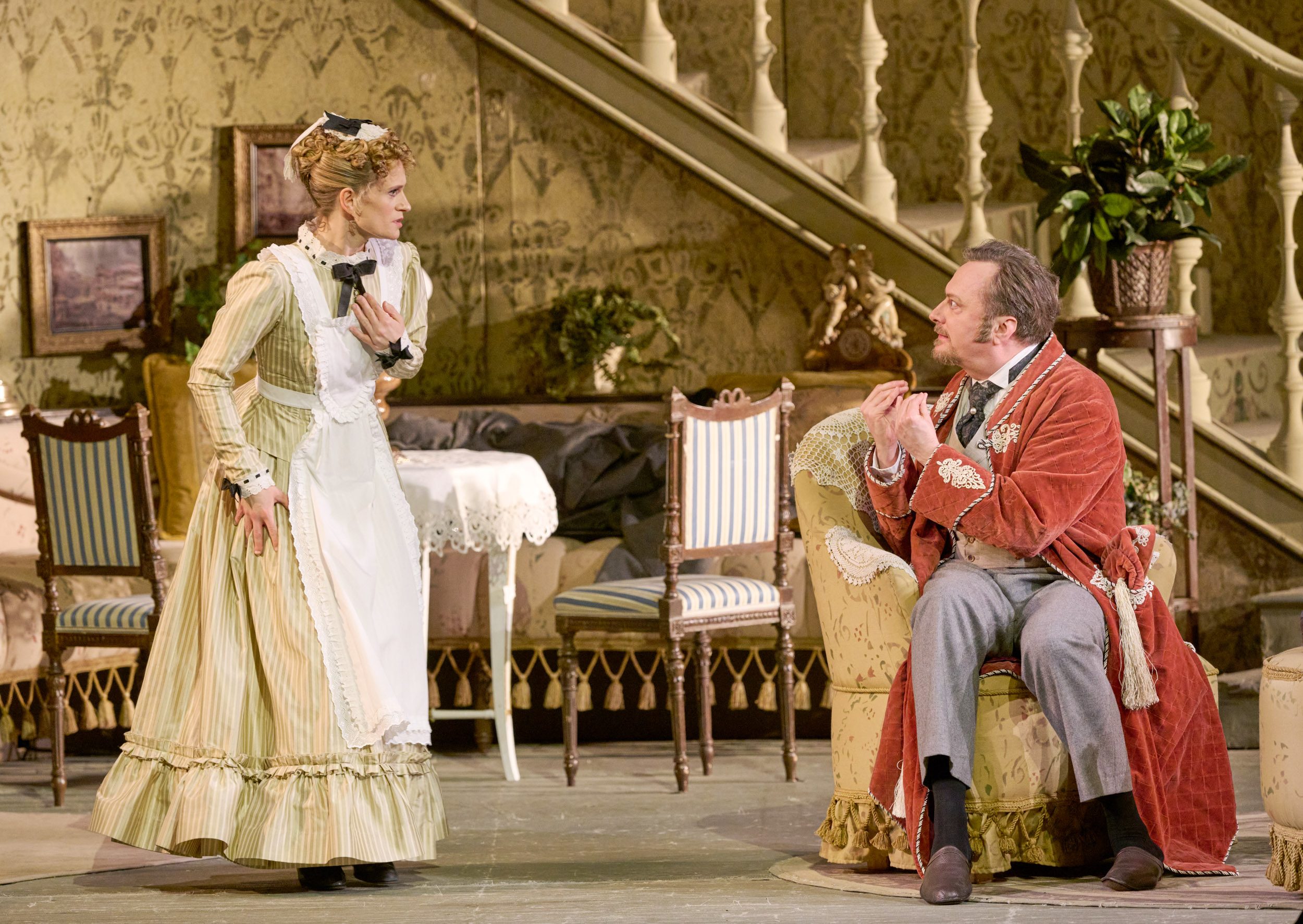 Eine Frau im Dienstmädchenkostüm blickt erschrocken auf eine sitzende Person in rosa Kleidung.