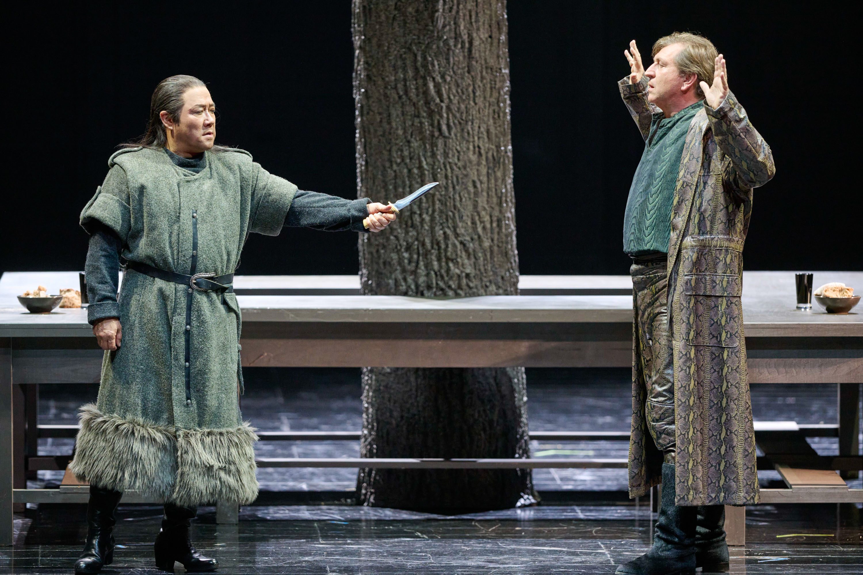 Zwei Menschen in mittelalterlicher Kleidung stehen sich auf einer Bühne gegenüber, einer davon hält ein Messer erhoben.