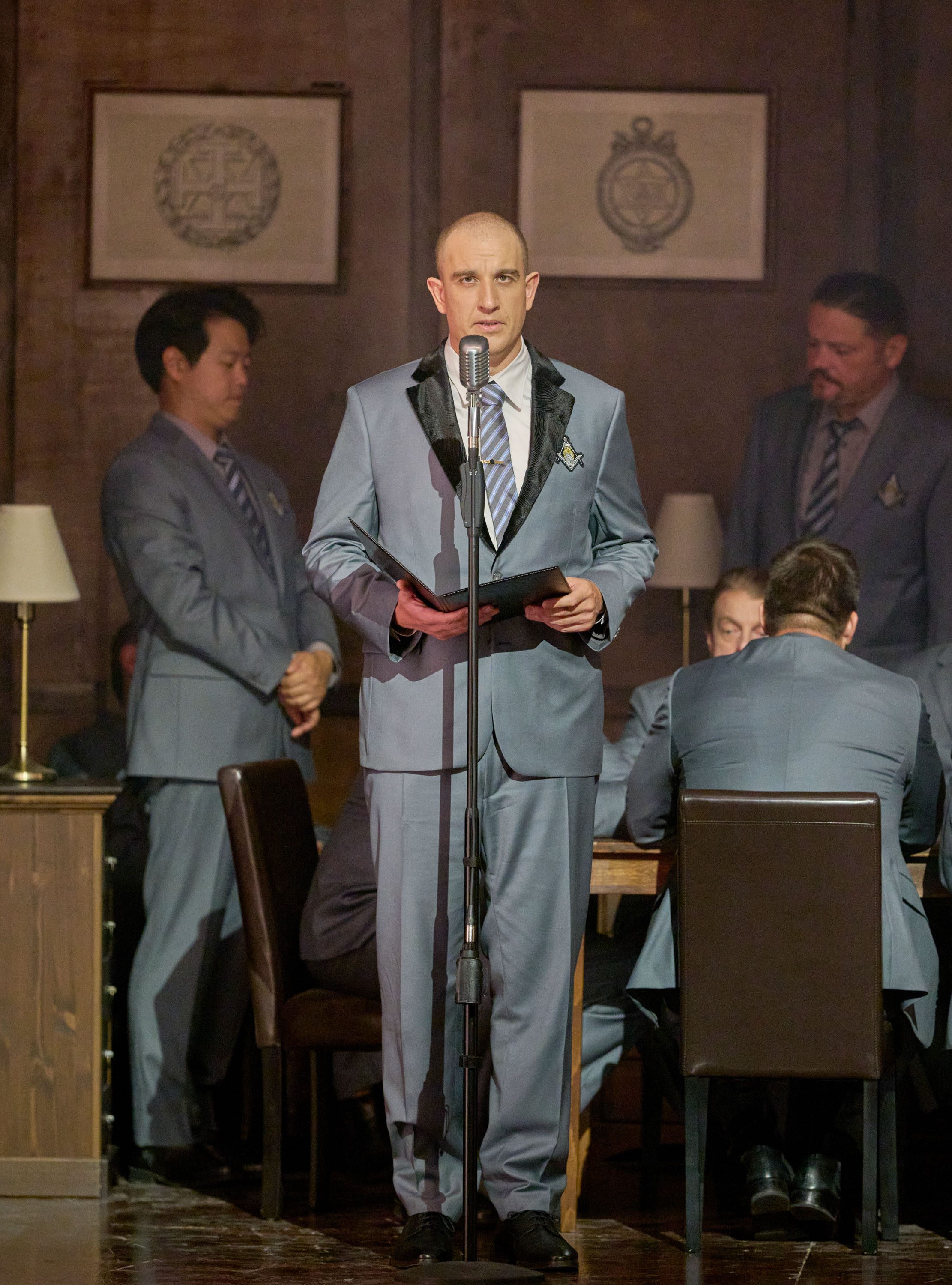 Ein Mann mit Glatze der einen grauen Anzug trägt steht vor einem Mikrofon und sagt etwas. In seinen Händen hält er ein Buch.