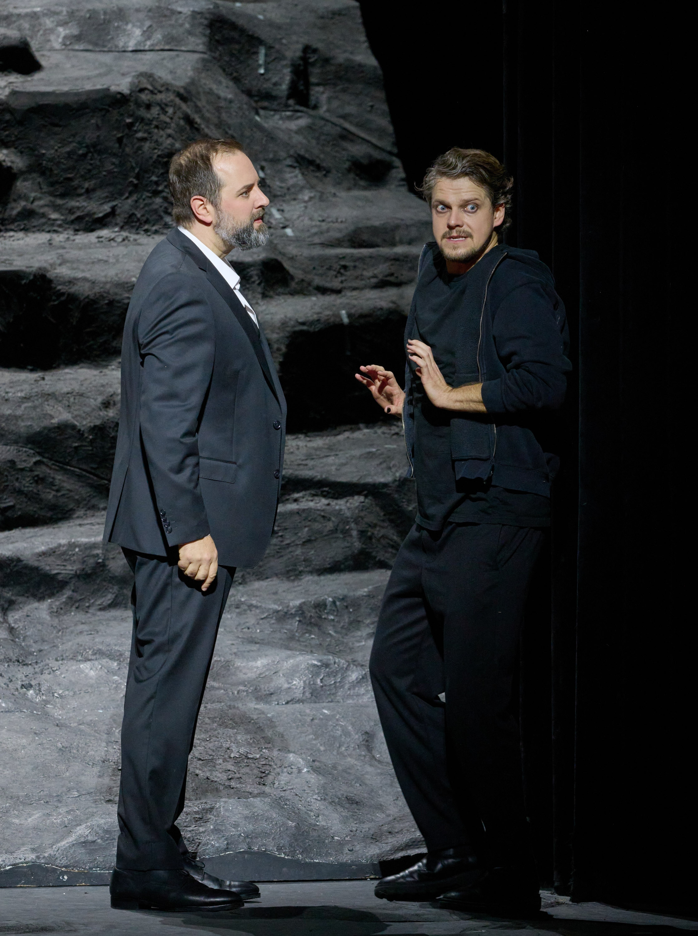Zwei Männer in dunklen Gewändern stehen vor einer grauen Felsenlandschaft.