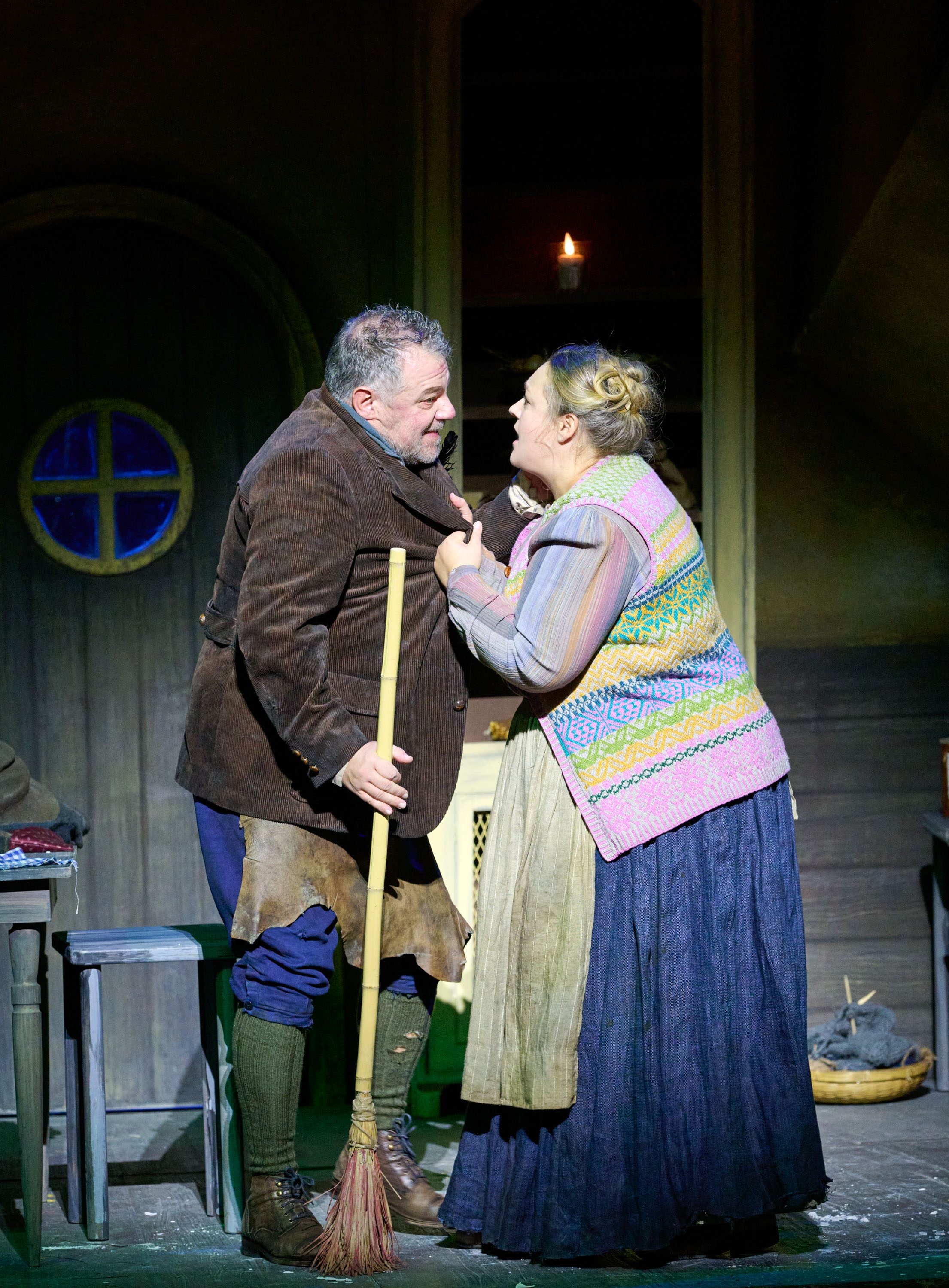 Zwei Darsteller in rustikaler Kleidung stehen sich in einer Hütte gegenüber, gestikulieren lebhaft und wirken emotional aufgebracht.