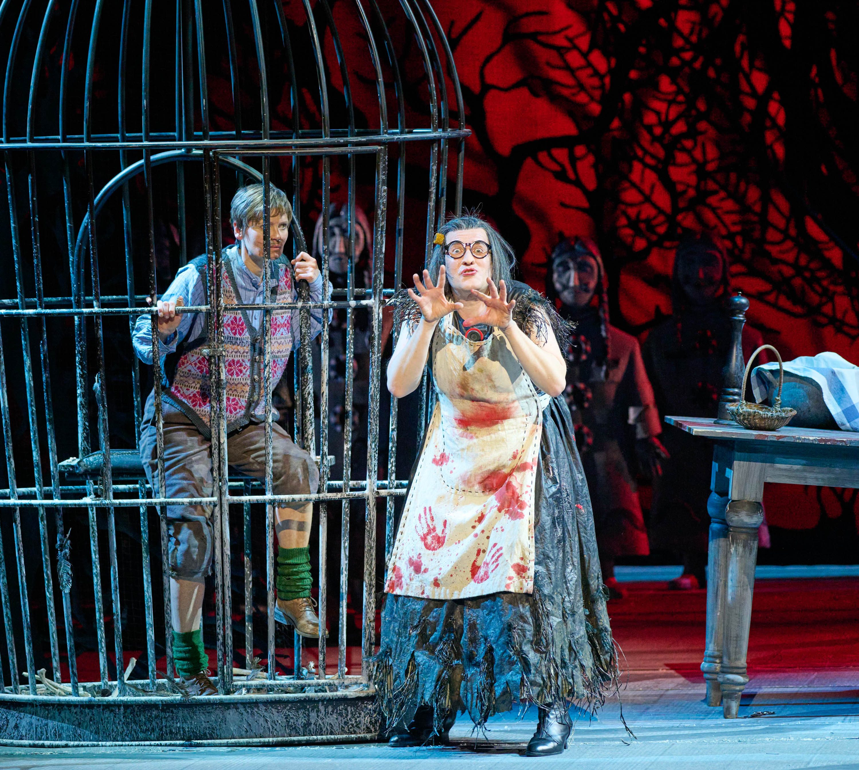 A character in a bloodstained apron gestures dramatically while standing near a table. In a cage behind her, another character appears trapped and looks anxiously towards her. The scene conveys a sense of tension and drama, set against a dark, ominous background.