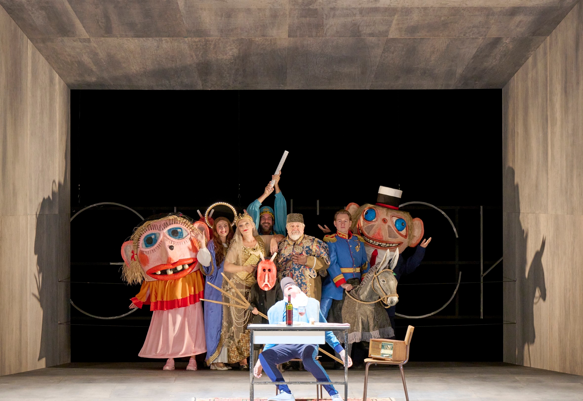 Eine bunt gekleidete Gruppe beobachtet einen an einem Tisch sitzenden Mann von hinten.