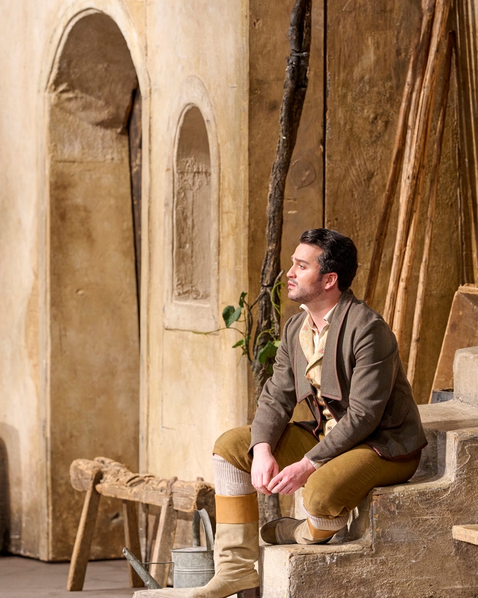 Ein Mann in historischer Kleidung sitzt nachdenklich auf einer Treppe vor einer mediterranen Hausfassade.