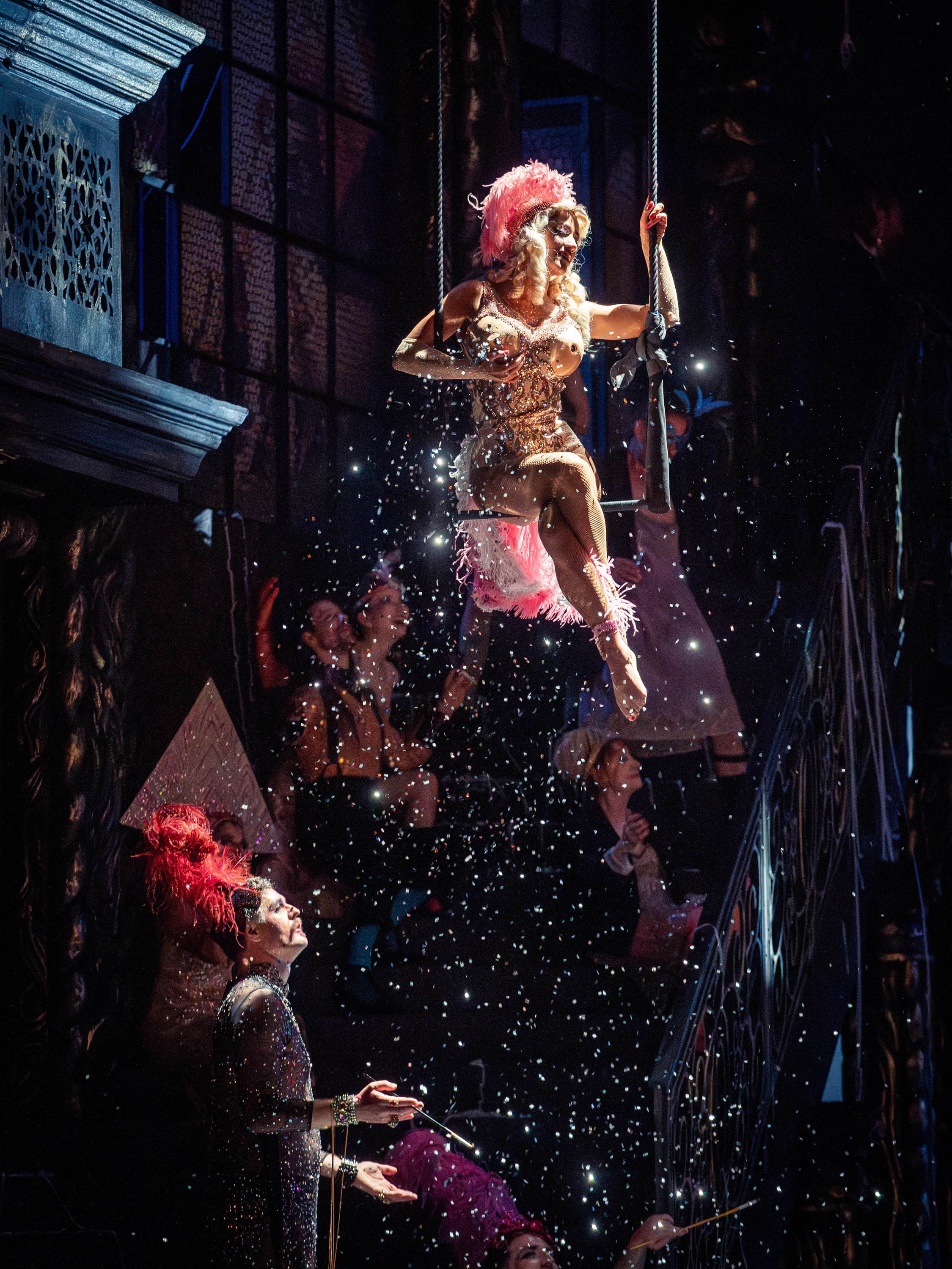 Eine Frau sitzt in einem Glitzerkostüm sitzt auf einer Schaukel. Aus ihren Brüsten kommt Glitzer.