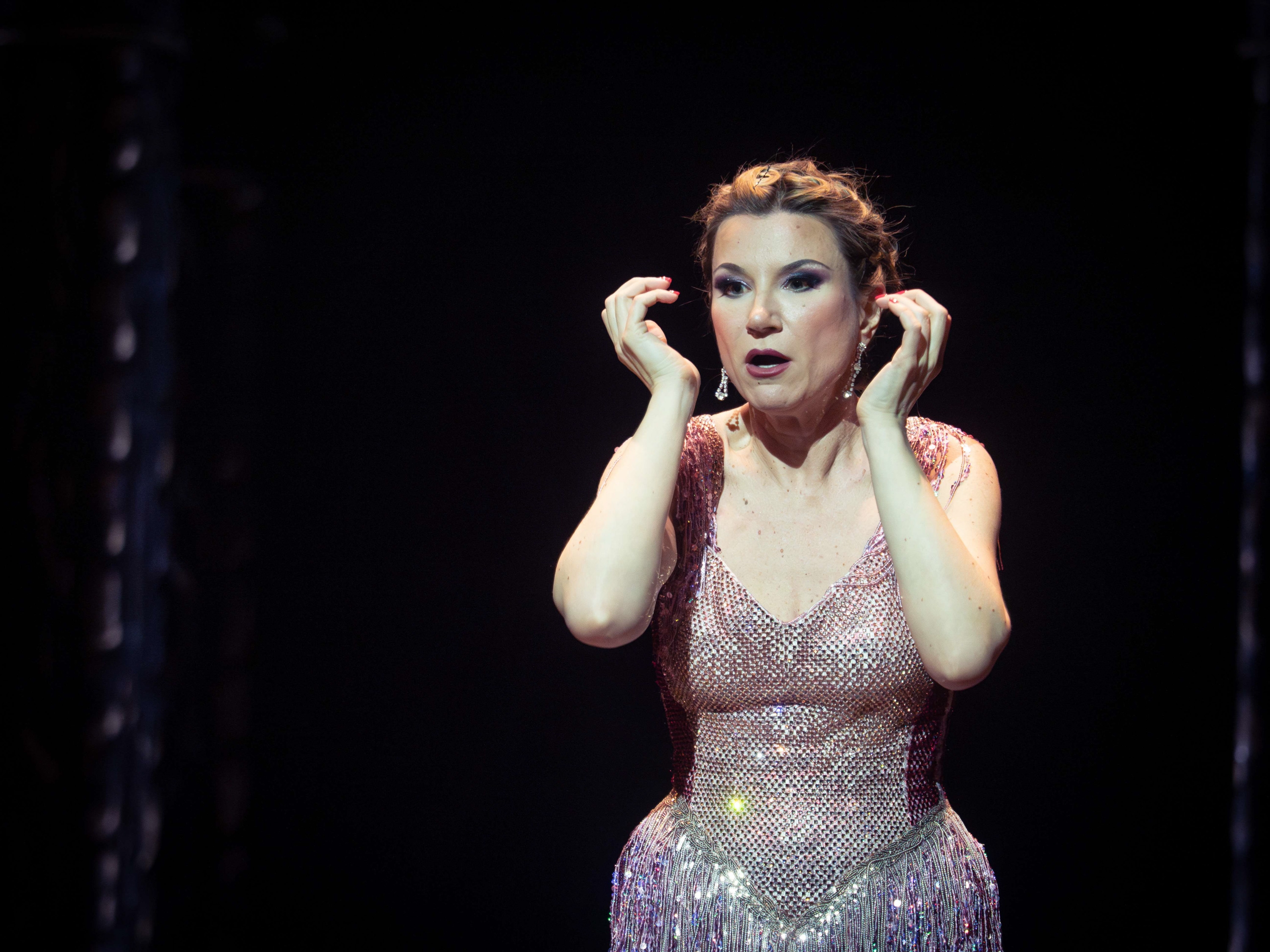 Eine Frau in einem Rosa Glitzerkostüm steht vor einem schwarzen Hintergrund.