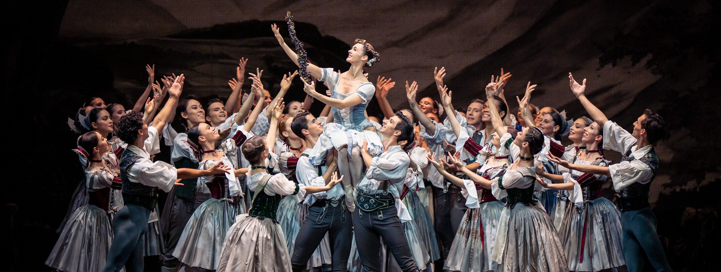 Eine Tanzgruppe in festlicher Tracht zeigt eine beeindruckende Aufführung. Eine Tänzerin wird von anderen Tänzern umgeben, die ihre Hände heben und sie triumphierend anfeuern. Die Atmosphäre ist voller Energie und Begeisterung, die den Höhepunkt des Auftritts unterstreicht.